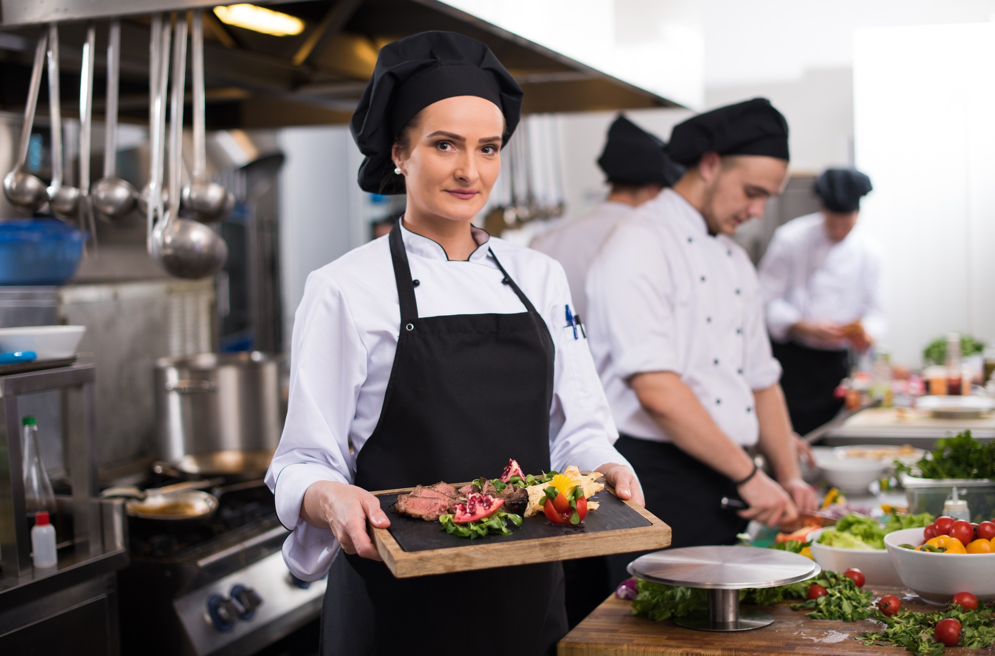 Female Chef In Hotel or Restaurant Kitchen Holding Grilled Beef Steak Plate With Vegetable Decoration.